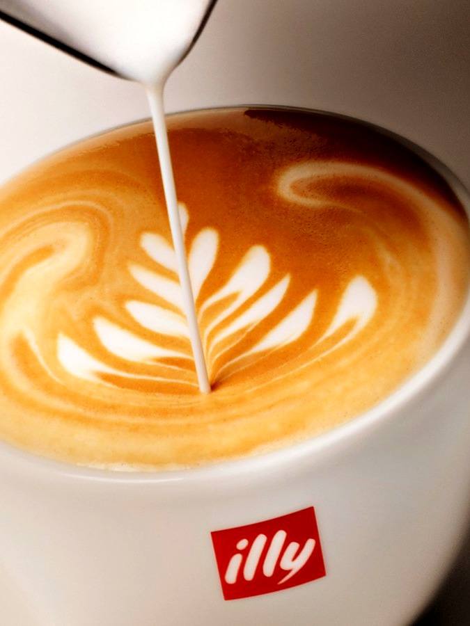 Milchschaum wird in eine illy-Tasse gegossen, auf dem Cappuccino entsteht ein Latte-Art-Blatt