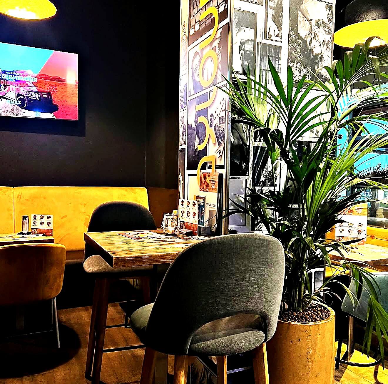 Ecke mit Palme, grauen Stühlen, Holztisch und senfgelber Sitzbank